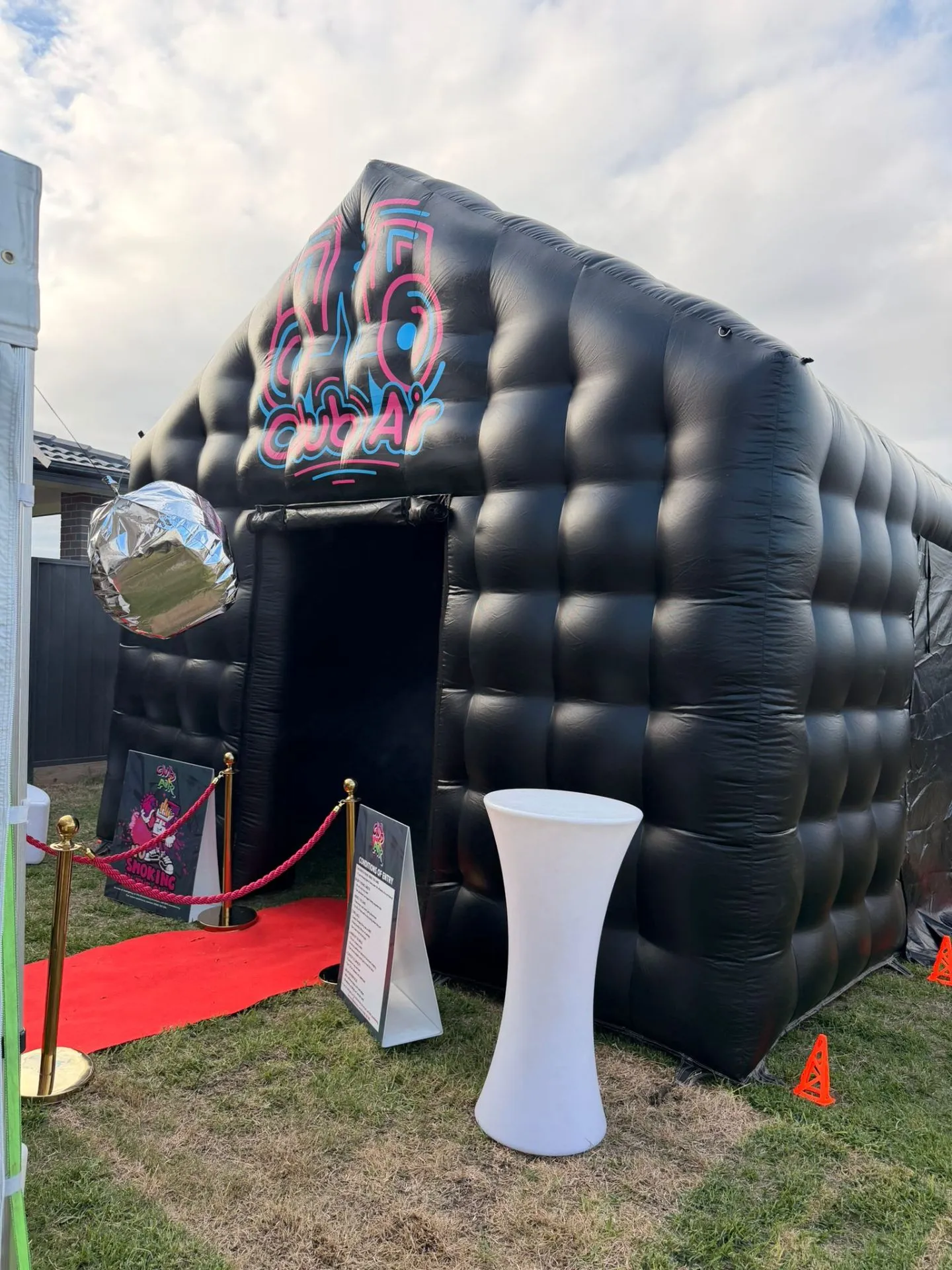 Side angle of the Club Air inflatable nightclub with a hanging disco ball, white cocktail table and neon Club Air logo, Sydney
