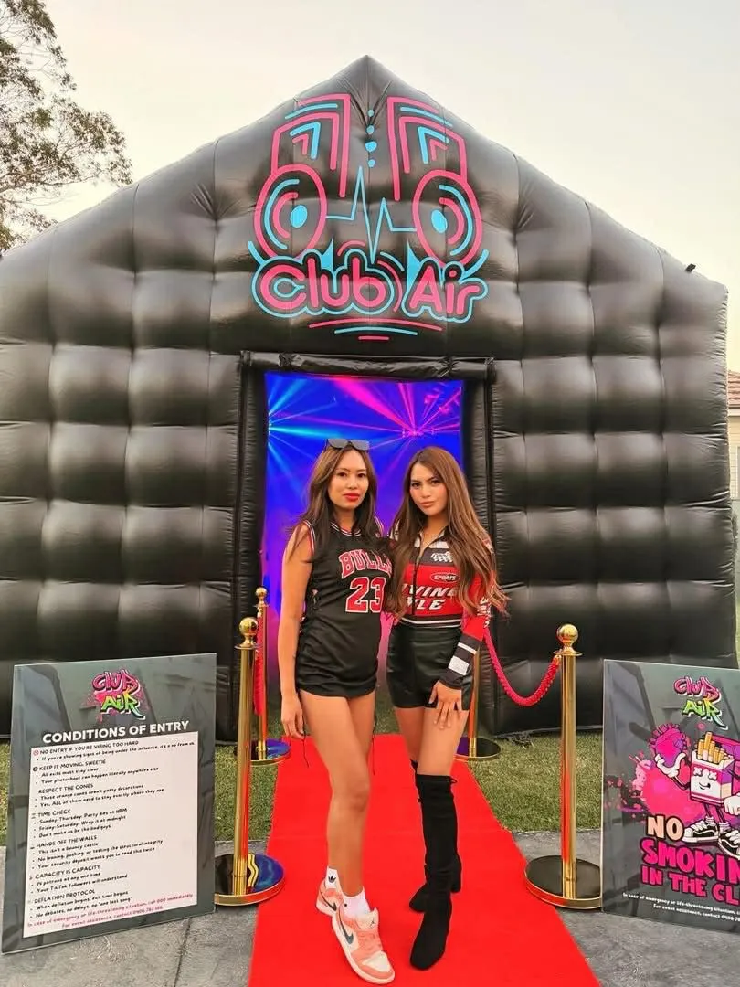 Two party guests posing on the red carpet in front of the Club Air inflatable nightclub at sunset, Sydney